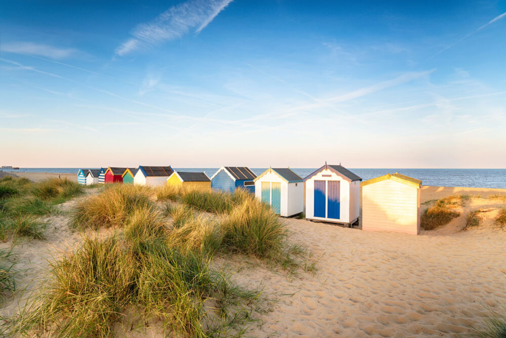 Brightly coloured beach huts grace the sand and dunes on a sunny day