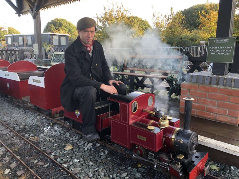 A train driver sits at the front of the miniature steam locomotive at Southwold Railway Trust