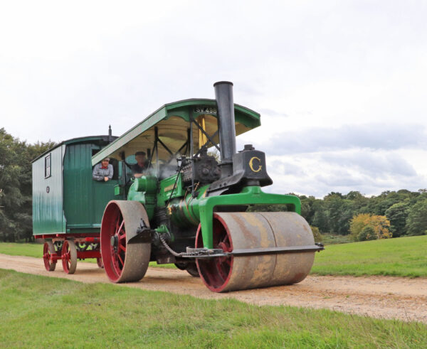 A green steam roller pulls a green caravan behind it