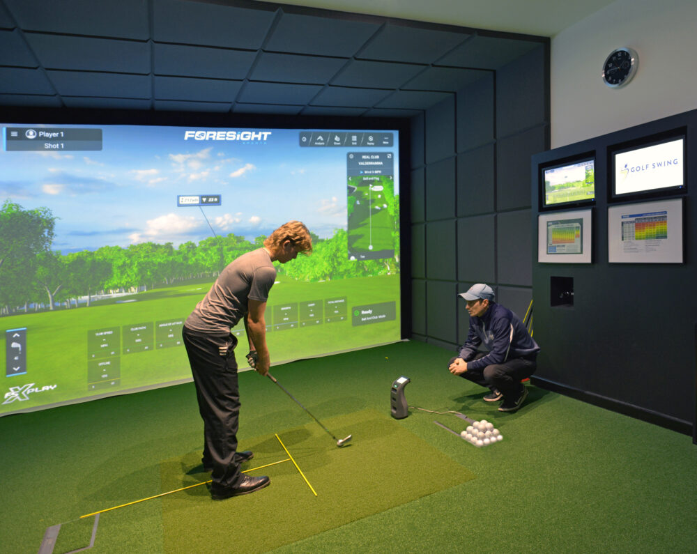 Two golfers practising shots with the Foresight golf simulator